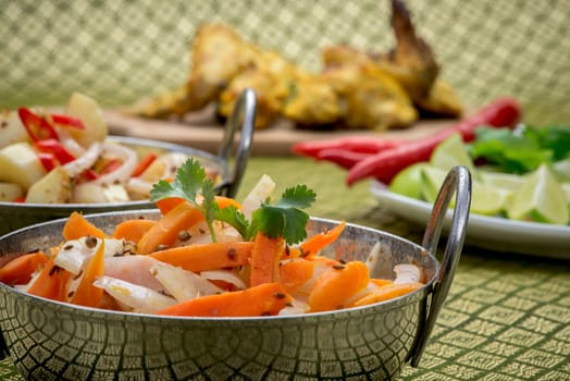 Indian chicken on a platter with bowls of salad and a garnish of lime, corriander and chili