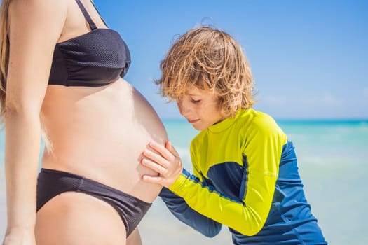 A radiant pregnant mother and her excited son share a tender moment on a serene, snow-white beach, celebrating family love amidst nature's beauty.