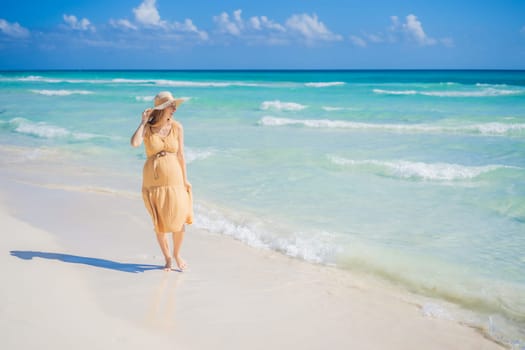 Radiant and expecting, a pregnant woman stands on a pristine snow-white tropical beach, celebrating the miracle of life against a backdrop of natural beauty.