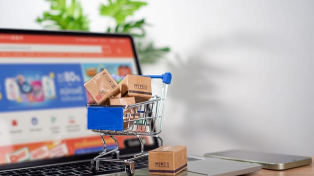 Shopping cart and product boxes placed on laptop computer represent online shopping concept, website, e-commerce, marketplace platform, technology, transportation, logistics and online payment concept.