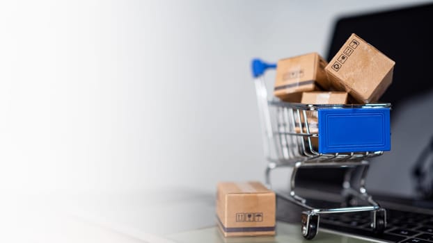 Shopping cart and product boxes on laptop computer on white background and copy space. online shopping marketplace platform website E-commerce technology, shipping, logistics and online payment concepts.