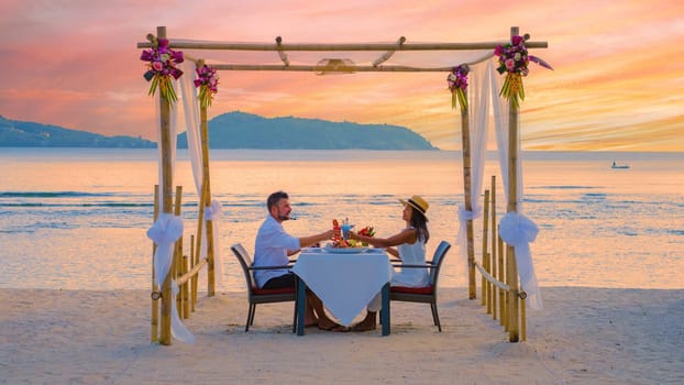 Romantic dinner on the beach in Phuket Thailand, couple man and woman mid age Asian woman and a European man having dinner on the beach in Thailand during sunset during a luxury holiday vacation