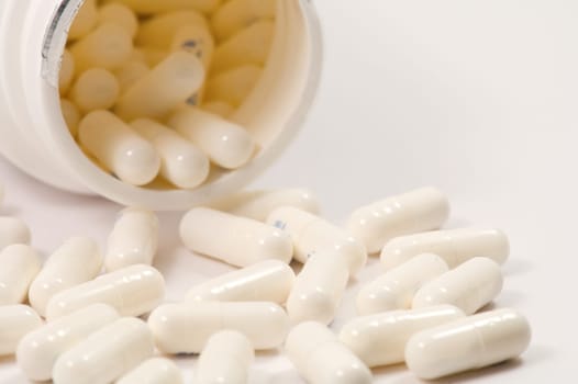 Open bottle of of medical capsules over white