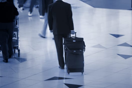 A man with suitcase rushing through the airport in blue tune