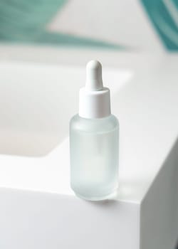 Clear glass dropper bottle with pipette on washbasin in green tropical bathroom close up, mockup. Natural unbranded cosmetics scene, copy space. Spa and facecare concept
