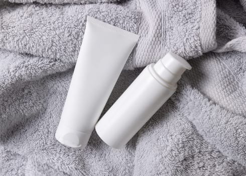 White blank cosmetic squeeze cream tube one pump bottle on light gray towel in bathroom top view, brand packaging mockup. Natural herbal cosmetic product for daily facecare, copy space