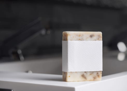 Beige handmade soap bar with blank label on washbasin near faucet in modern dark grey masculine bathroom close up, mockup. Natural herbal product for daily male hygiene and bodycare