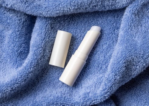 Opened white blank lip balm stick on blue bath towel, top view, cosmetic mockup. Lifestile scene with Lipcare beauty product for mens daily personal care