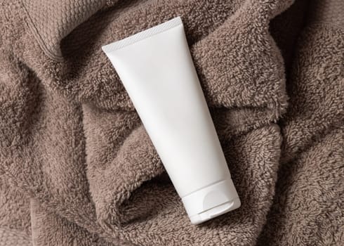 White blank squeeze cream tube on brown towel in bathroom top view, brand packaging mockup, copy space. Natural handmade cosmetic product for facecare and spa procedures