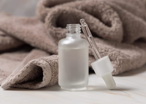 Pipette set near an opened clear glass glass dropper bottle filled with liquid near light brown bath towel close up, mockup. Natural serum or essence for daily beauty facecare