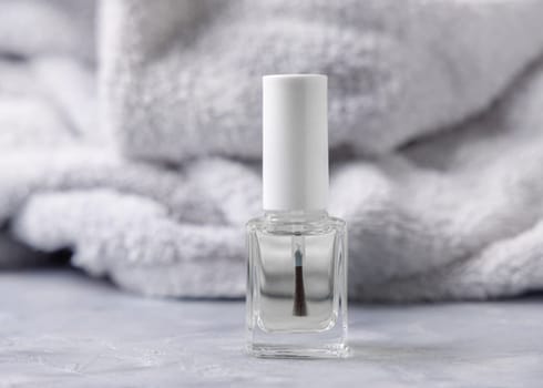 Clear glass refillable bottle with white blank brush cap near grey bath towel on grey close up, cosmetics mockup. Natural skincare nail product, minimal aesthetic