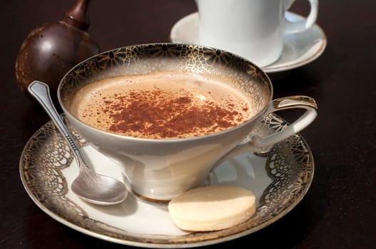 Fine porcelain cup with coffee, milk and sprinkled cinnamon on dark background