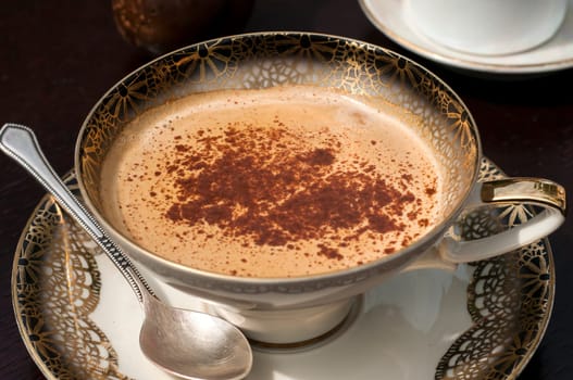 Fine porcelain cup with coffee, milk and sprinkled cinnamon on dark background