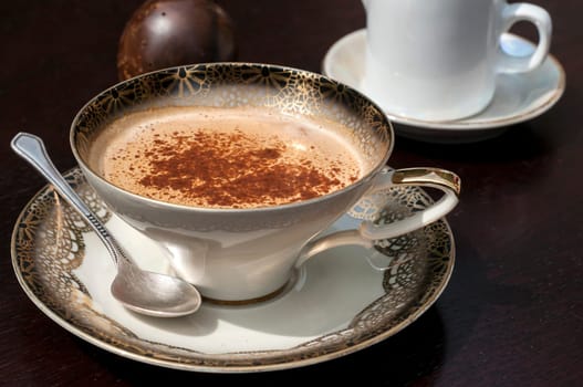Fine porcelain cup with coffee, milk and sprinkled cinnamon on dark background