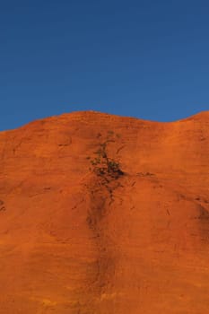 Red and orange ocher hill with blue sky in the background. 2/3 hill and 1/3 blue sky. Le Colorado Provencal de Rustrel (France). Vertically.