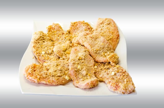 Breaded schnitzel on a white plate with grey white background.