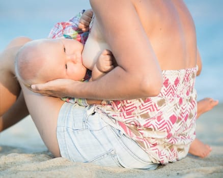 Mother breastfeeding baby on the beach
