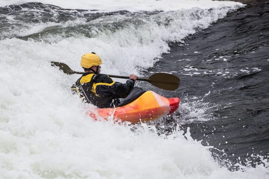 an active male kayaker rolling and surfing in rough water