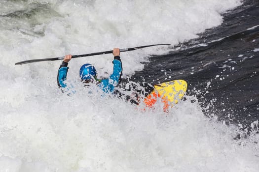 an active male kayaker rolling and surfing in rough water