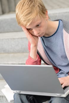 Bored teenage student using laptop sitting outside on steps