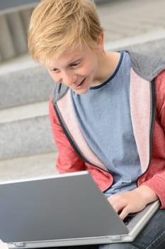 Surprised teenage student boy using laptop sitting outside on steps
