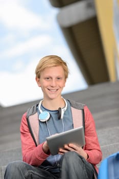 Happy teenage boy using tablet sitting on steps outdoors