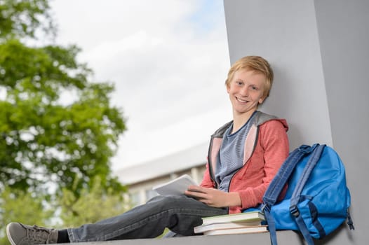 Happy teenage boy studying on wall outside his school campus
