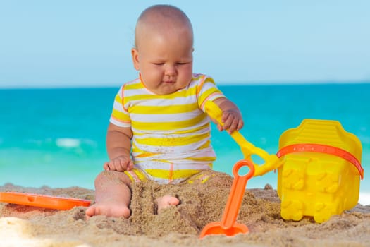 Cute baby on the tropical beach playing toys
