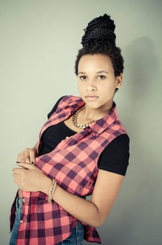 Young african girl with black dreadlocks wearing trendy hip-hop fashion and posing in front of a grey wall.