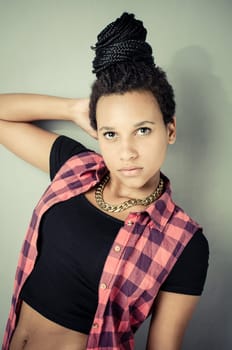 Young african girl with black dreadlocks wearing trendy hip-hop fashion and posing in front of a grey wall.