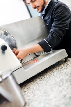 chef cuts fresh ham on the cutting machine in the restaurant kitchen