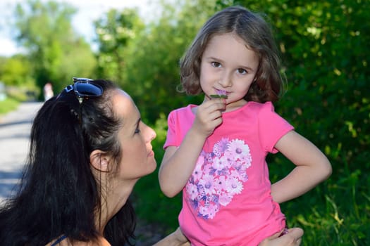 Little girl smelling a flower while walking with her mother