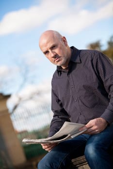 adult older man sitting outdoors reads a newspaper news free time