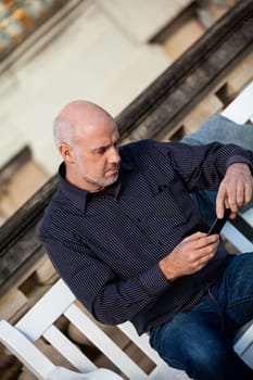 Attractive older man senior with mobile phone smartphone on a bench in the park in summer