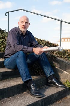 Middle-aged man,senior sitting with a newspaper on a staircase in spring outdoors