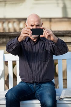 Attractive older man senior photographs himself with his mobile phone smartphone in the park