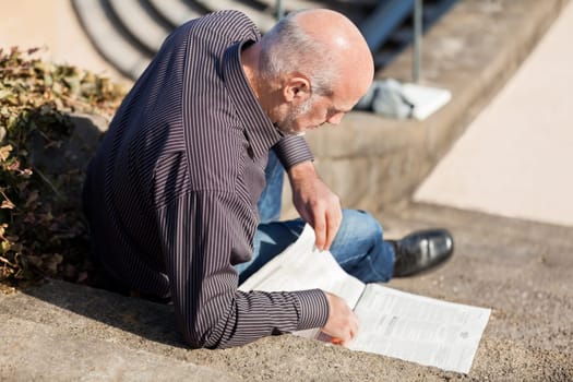 Middle-aged man,senior sitting with a newspaper on a staircase in spring outdoors