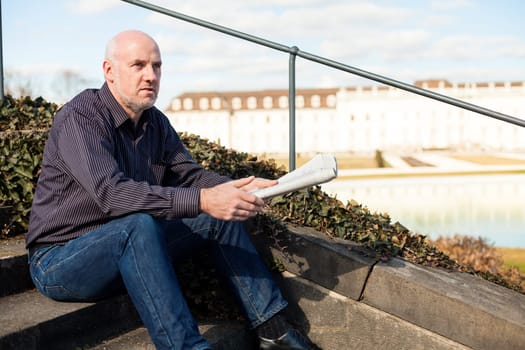 Middle-aged man,senior sitting with a newspaper on a staircase in spring outdoors
