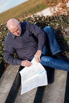 Middle-aged man,senior sitting with a newspaper on a staircase in spring outdoors