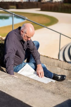 Middle-aged man,senior sitting with a newspaper on a staircase in spring outdoors