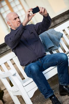 Attractive older man senior photographs himself with his mobile phone smartphone in the park