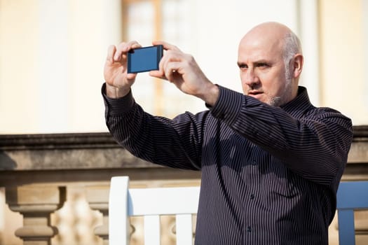 Attractive older man senior photographs himself with his mobile phone smartphone in the park