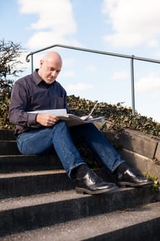 Middle-aged man,senior sitting with a newspaper on a staircase in spring outdoors