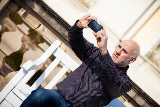 Attractive older man senior photographs himself with his mobile phone smartphone in the park