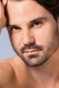 Young naked man with dark hair and beard as a portrait against a grey background