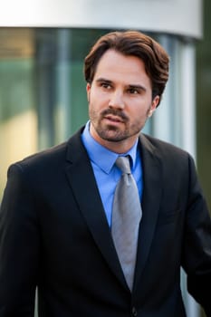 Young trendy businessman in front of a business building successfully with beard and dark hair