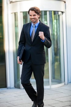 Attractive young businessman cheering in front of a business building in the summer