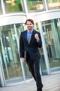 Attractive young businessman cheering in front of a business building in the summer