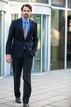 Young trendy businessman in front of a business building successfully with beard and dark hair