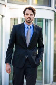 Young trendy businessman in front of a business building successfully with beard and dark hair